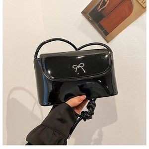Detail of glossy black patent leather shoulder bag with a silver bow metal buckle