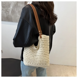 Detail of hand-woven cream bucket bag with brown leather strap and metal rivets on model