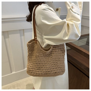 Detail of hollow woven straw tote bag with brown leather straps and gold metal rivets