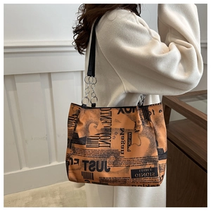 Detail of trendy orange tote bag with black letter print and metal chain shoulder strap