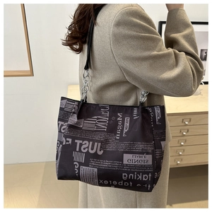 Detail of printed tote bag with silver chain strap and newspaper motif on black fabric