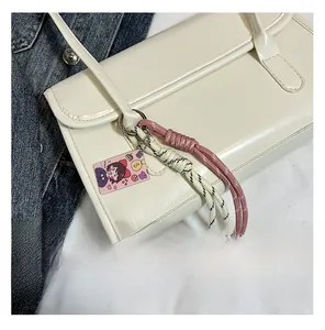Détail du sac cabas en similicuir blanc avec pompon en corde tressée et charme de dessin animé