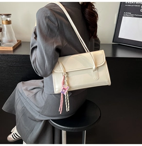 Detail of cream glossy leather underarm bag with colorful tassel and doll pendant charms