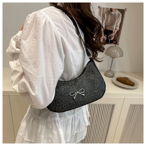 Detail view of black glitter shoulder bag with silver bow on a white lace dress model