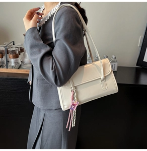 Detail of cream underarm bag featuring glossy PU leather and decorative pink tassel charm
