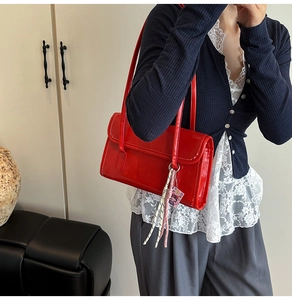 Detail of bright red patent leather tote bag featuring a decorative cartoon charm and strap