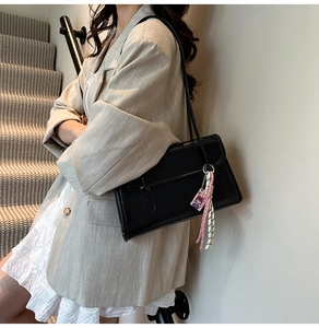 Detail of black faux leather shoulder bag with cute pink doll charm and striped knot decoration