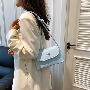 Light blue crossbody square bag with silver bow accent on a white blazer model