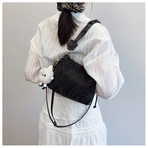 Detail of black pleated bucket bag with adjustable strap and white plush charm on model