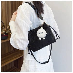 Detail of a black ruched bucket bag with a plush monster charm on a wooden shelf