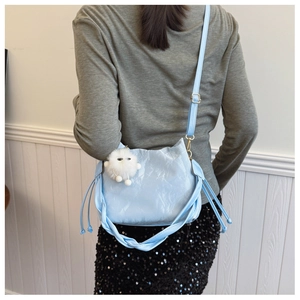 Detail of light blue pleated bucket bag with fluffy white plush charm and gold buckle