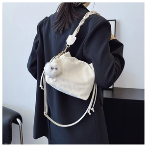 Detail of off-white pleated bucket bag with plush monster charm and woven strap on model