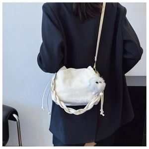 Detail of white drawstring bucket bag featuring a woven handle and plush ball charm accessory
