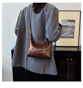Detail of dark brown leather crossbody bag with embossed logo and golden buckle