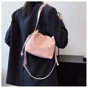 Pink pleated bucket bag with braided strap shown on shoulder over a black blazer