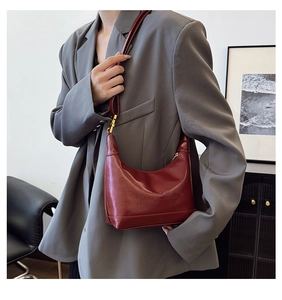 Detail of burgundy leather crescent bag with embossed logo and gold hardware on model