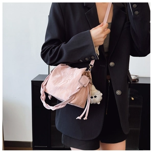 Detail of pink pleated bucket bag with braided handle and plush charm on black blazer