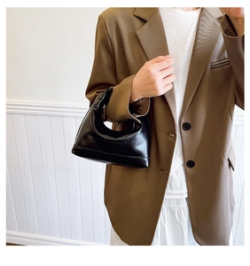 Detail of black leather hobo bag with St. Louise embossed text on a brown blazer background