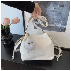 Detail of white drawstring bucket bag with plush charm and golden hardware accents