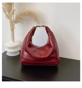 Close-up of burgundy patent leather baguette bag with gold buckle and embossed logo detail