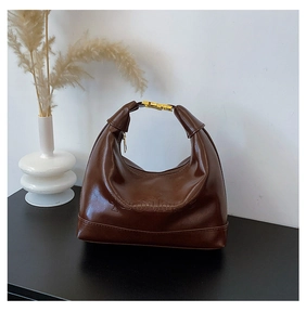 Detail of vintage brown leather hobo bag with gold hardware on a minimalist black stand