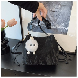 Detail of black pleated bucket bag with plush charm and long shoulder strap