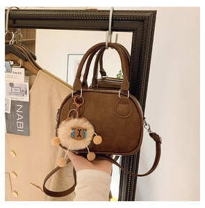 Detail of a brown bowling handbag with LUCKY WHO embossing and a cute plush bear charm
