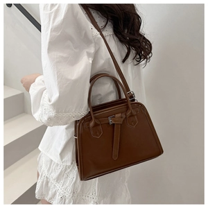 Detail of a brown leather tote bag showing a metal buckle and adjustable shoulder strap