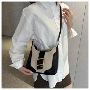 Détail du sac selle en toile et cuir noir avec boucle dorée porté par un mannequin