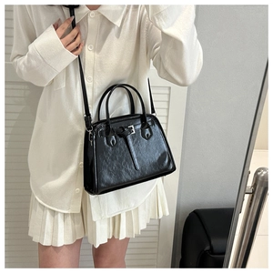 Fashionable black glossy trapezoid handbag with decorative buckle worn by a model