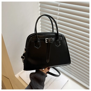 Detail of black glossy leather handbag with silver buckle held against aesthetic background