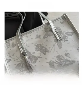 Detail of silver tote bag featuring butterfly embroidery and grey tassel ornament