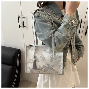 Detail of silver tote bag with butterfly prints and grey tassel on shoulder strap