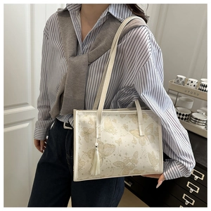 Close-up of white tote bag with golden butterfly pattern and decorative tassel detail