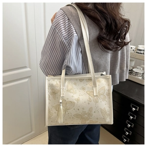 Detailed view of cream tote bag with butterfly print and tassels on a model shoulder