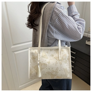 Close-up of beige tote bag featuring golden butterfly patterns and white tassel detail