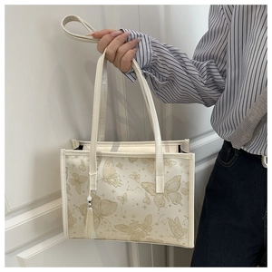 Detail of white tote bag with gold butterfly prints and tassel charm held by hand