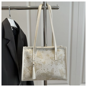 Close-up of beige tote bag with golden butterfly print and elegant tassel detail
