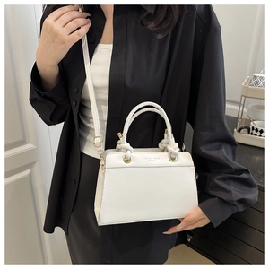 Detail of white trapezoid handbag featuring woven rope handles and gold-tone hardware