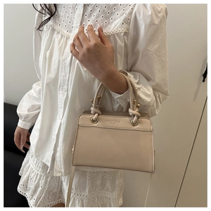 Detail of a cream faux leather tote featuring twisted top handles and fashion engraving