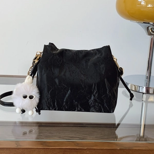 Minimalist black pleated bucket bag with a cute white plush monster charm on a glass table