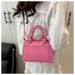 Detail of pink faux leather handbag featuring embossed logo and stylish knot handle
