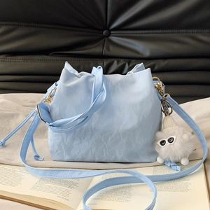 Light blue drawstring cloud bucket bag with plush cat charm on black quilted background