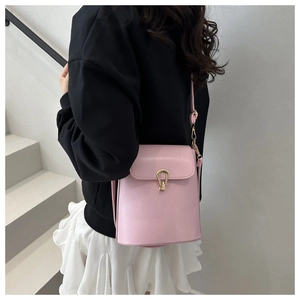 Detail of soft pink crossbody bucket bag with golden horseshoe lock on a model