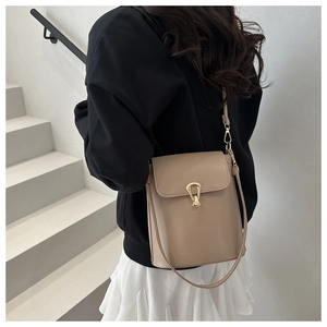 Model view of khaki crossbody bucket bag with gold horseshoe buckle on white stairs