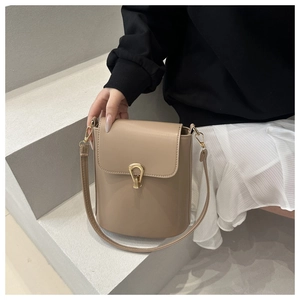 Detail view of khaki mini bucket bag with gold U-shaped hardware and a tassel accent