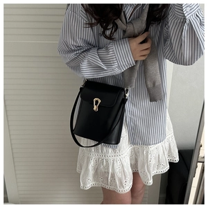Detail of black leather bucket bag with a gold horseshoe buckle on model for daily commute