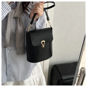 Detail of minimalist black crossbody bag with gold teardrop clasp and leather texture