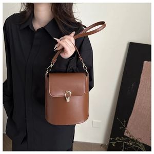 Close-up of brown leather bucket bag featuring a polished gold horseshoe buckle clasp