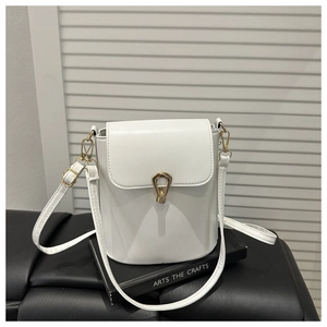 Detailed view of white bucket bag with gold metal swivel lock on a black book